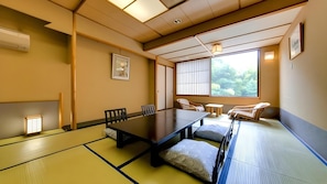 Una habitación con esteras tatami, una mesa baja, sillas y vistas al exterior con vegetación.
