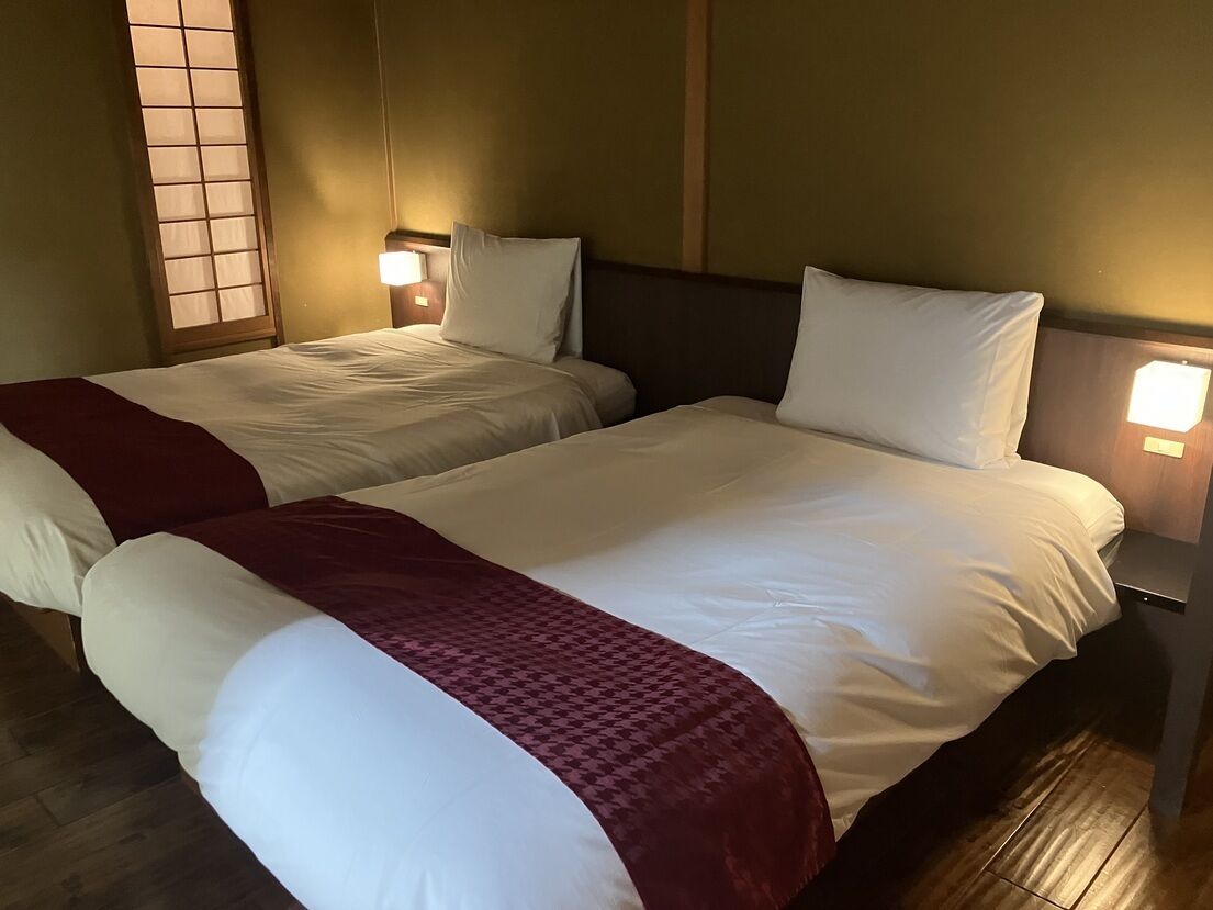 Un lit double avec une couvre-lit rouge et blanche, deux lampes de chevet et une fenêtre à motifs géométriques.
