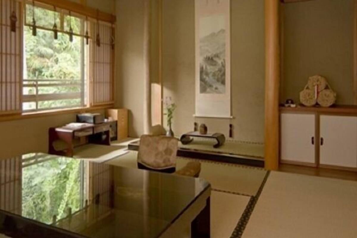 A traditional Japanese room with tatami flooring, a low table, a cushioned chair, a sliding door, and a wall-mounted cabinet.