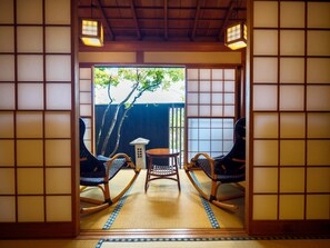 A traditional Japanese room with tatami flooring, a low table, two rocking chairs, and a view of a tree outside. - Izu Ito Hot Springs Toushinan Komeya-Kyoritsu Resort (Ito)