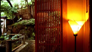 A traditional Japanese garden with a wooden fence, a stone path, and a lamp post. - Tousin-an Komeya (Ito)