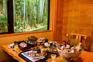 A dining table with various dishes, a bowl of sushi, and a view of bamboo forest through a window. - Izu Ito Hot Springs Toushinan Komeya-Kyoritsu Resort (Ito)
