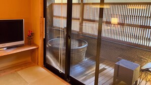 A room with a sliding glass door leading to an outdoor area, a television on a wooden shelf, and a small table with a chair. - Tousin-an Komeya (Ito)