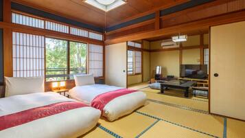 A traditional Japanese-style room with tatami flooring, two beds with white and red bedding, a television, and a sliding door leading to another room.