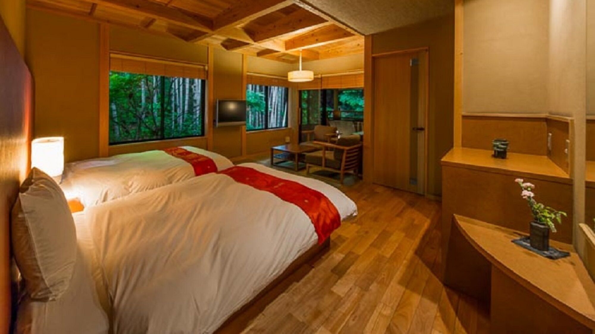 A room with two beds, a desk, a chair, a TV, and a view of trees through the window.