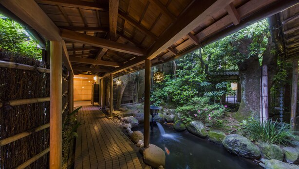 A covered walkway with a water feature, surrounded by rocks and greenery. - Tousin-an Komeya (Ito)