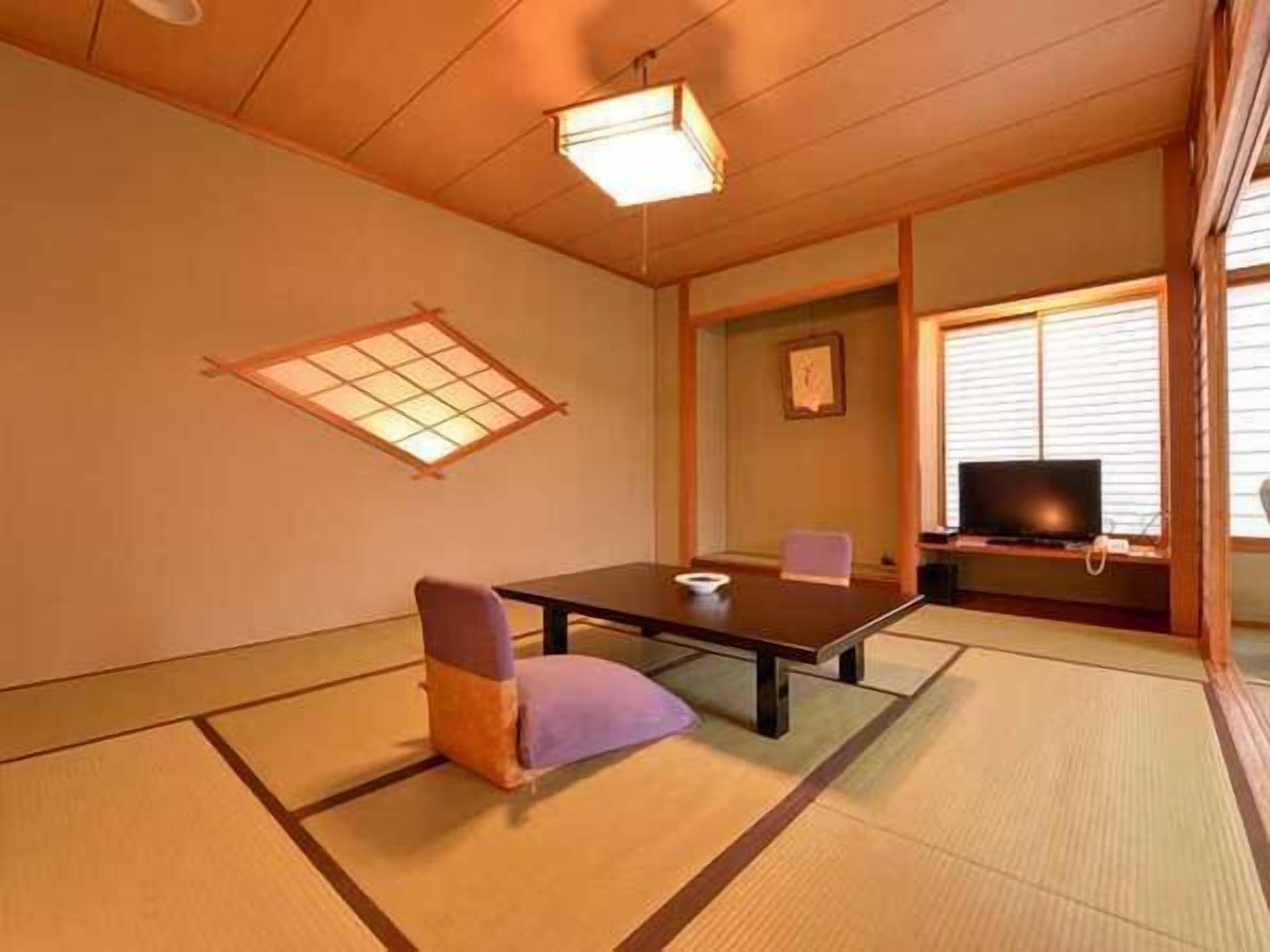 Una habitación japonesa tradicional con suelo de tatami, una mesa baja, un cojín, un televisor y un panel shoji.
