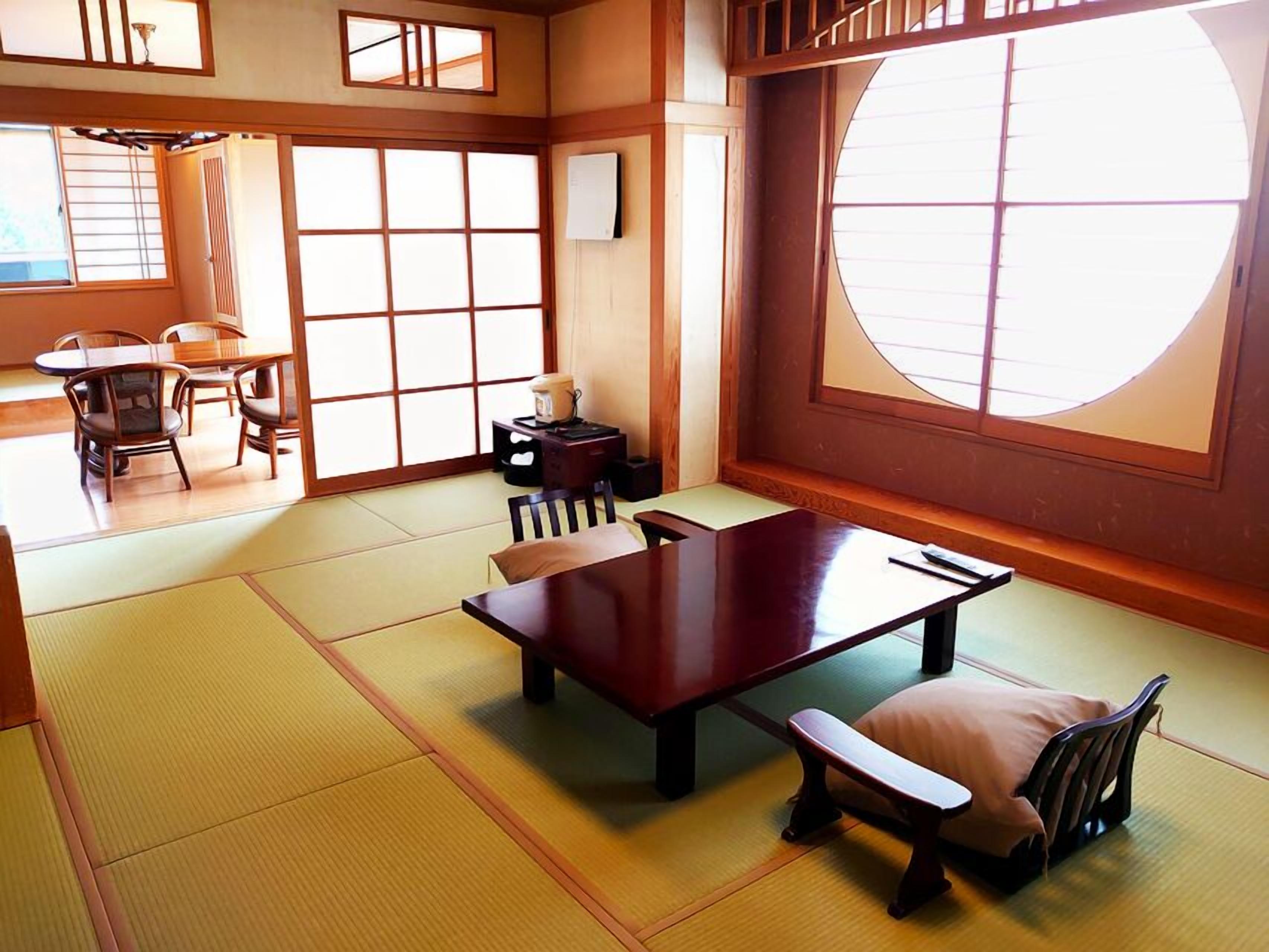 Ein Raum mit Tatami-Matten, inklusive Tatami-Tisch, Tatami-Sitzbank und traditioneller japanischer Einrichtung mit Schiebetüren und einem großen Fenster.