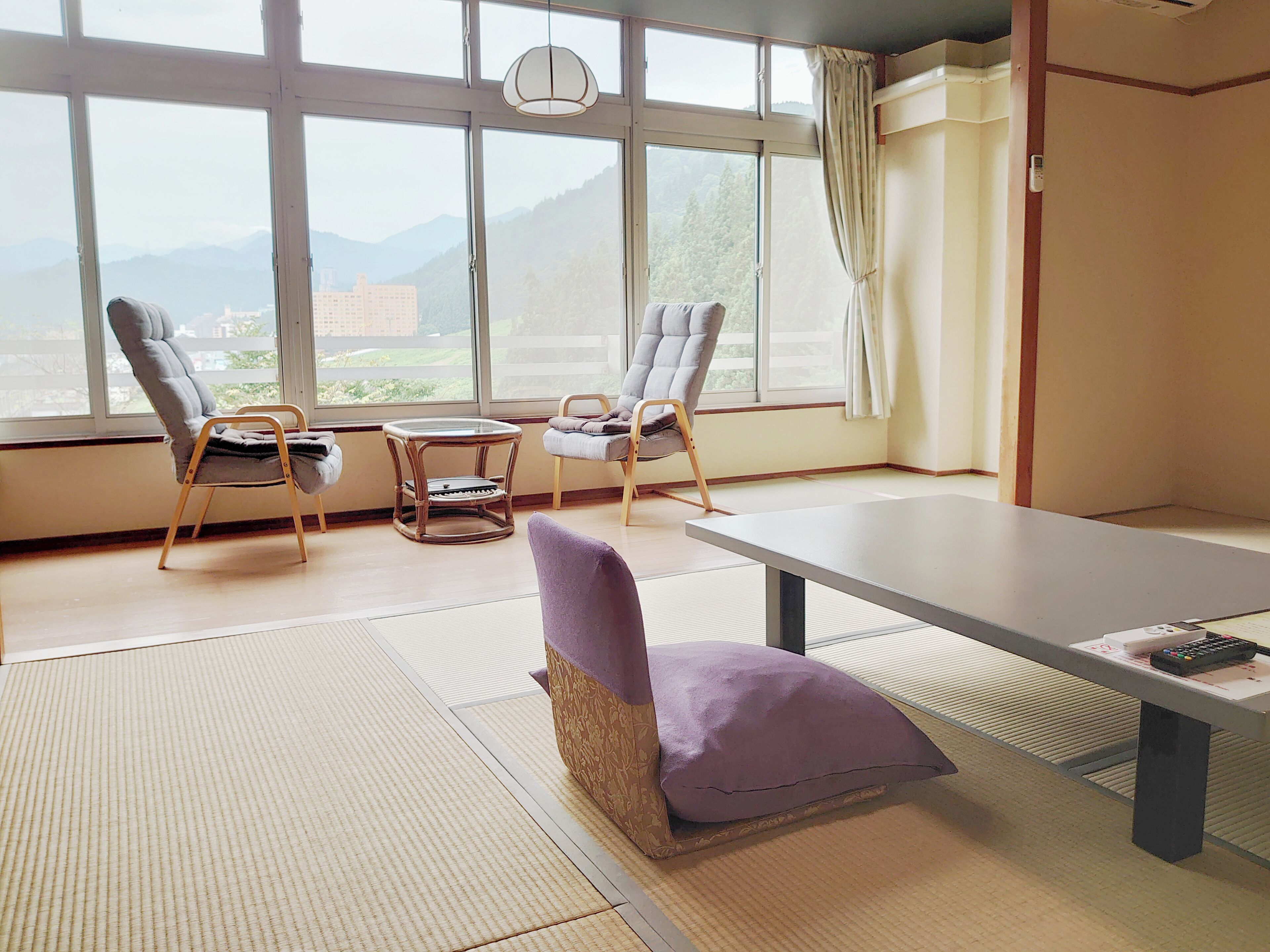 Una habitación con dos sillas, una mesita y un ventanal grande con vistas a montañas.