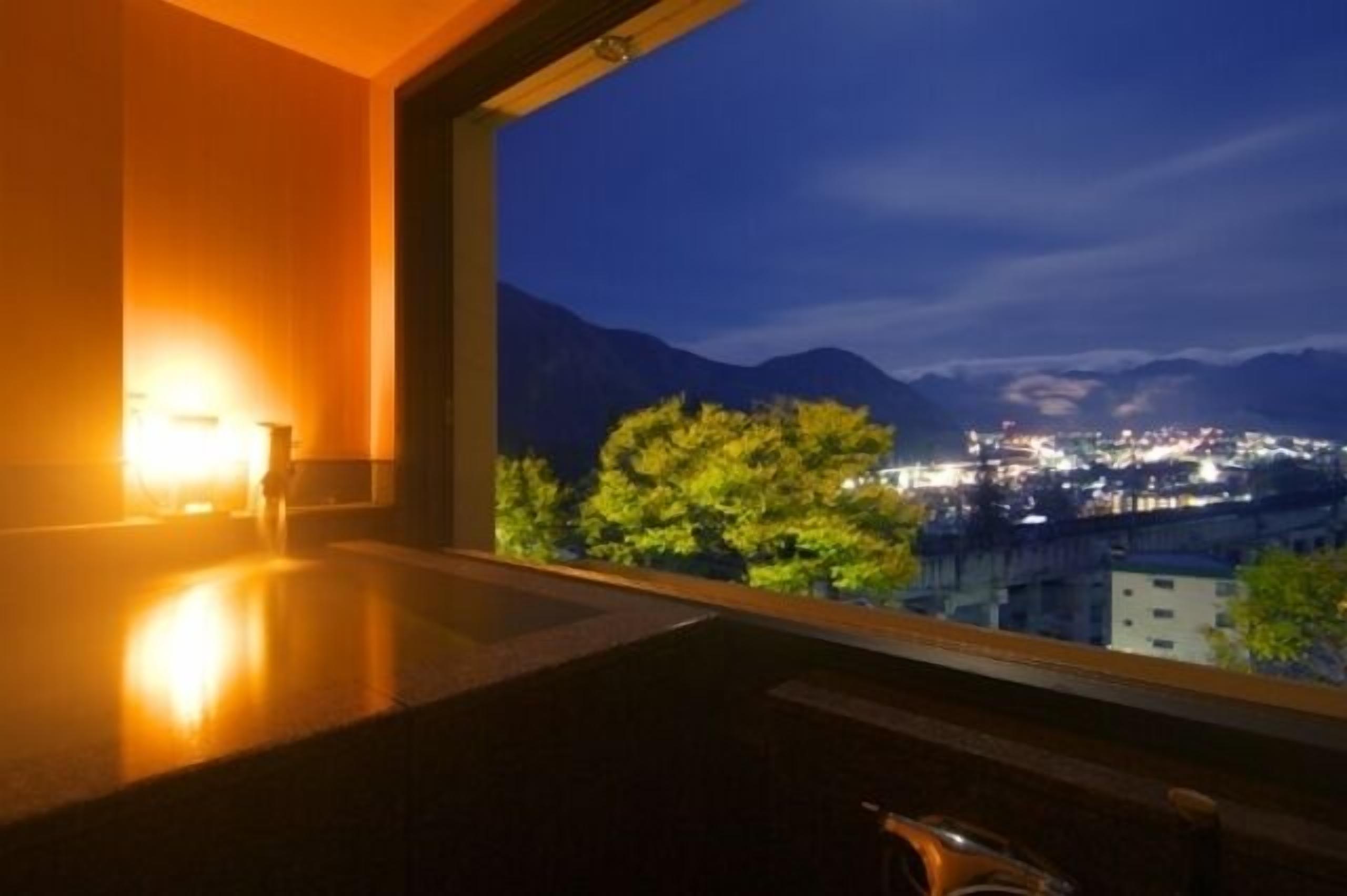 Habitación con un gran ventanal que da a un paisaje urbano nocturno, suelo de madera y una lámpara fijada a la pared.