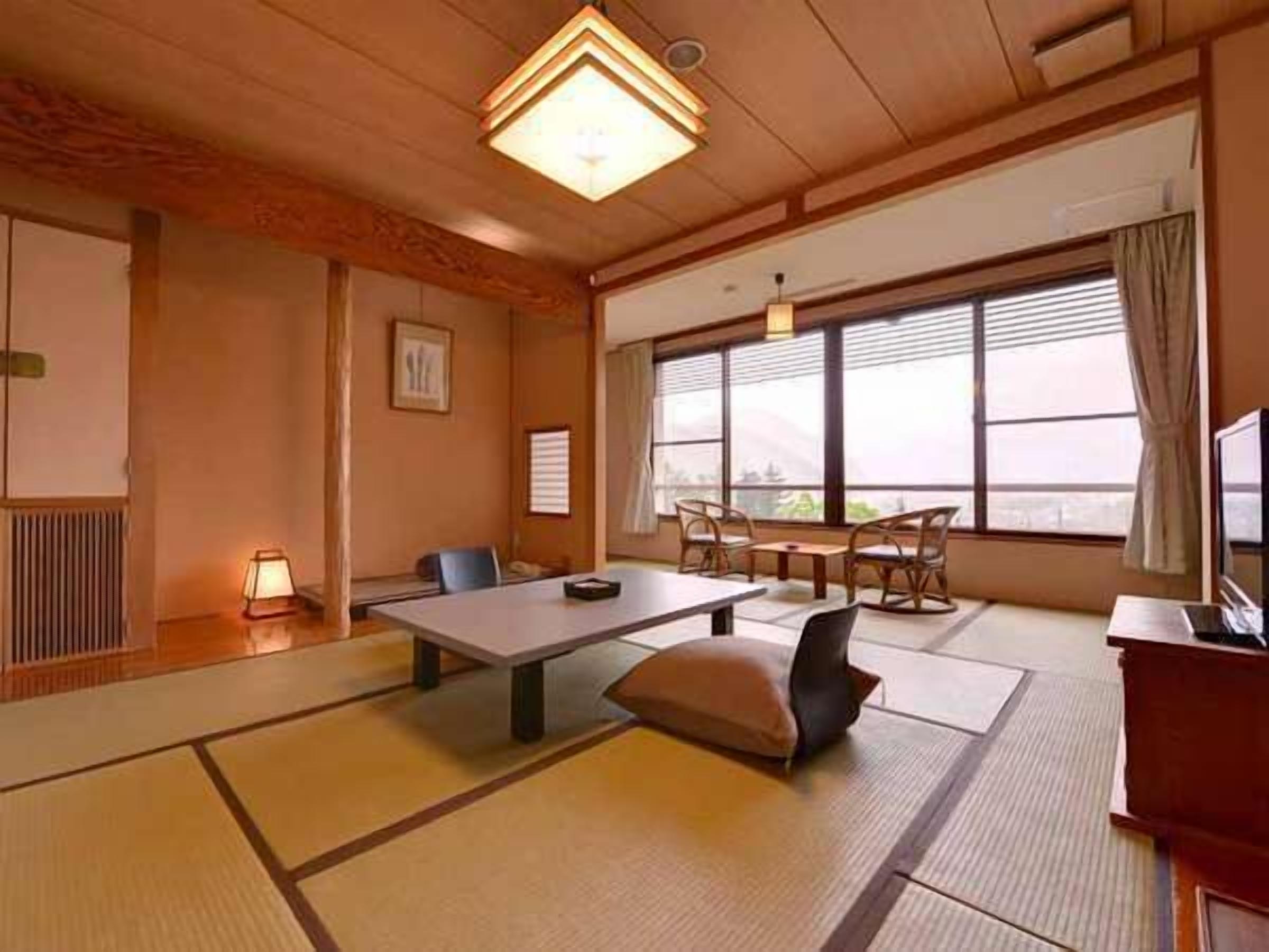Ein traditioneller japanischer Raum mit Tatami-Böden, einem niedrigen Tisch, Stühlen und einem großen Fenster mit Blick.