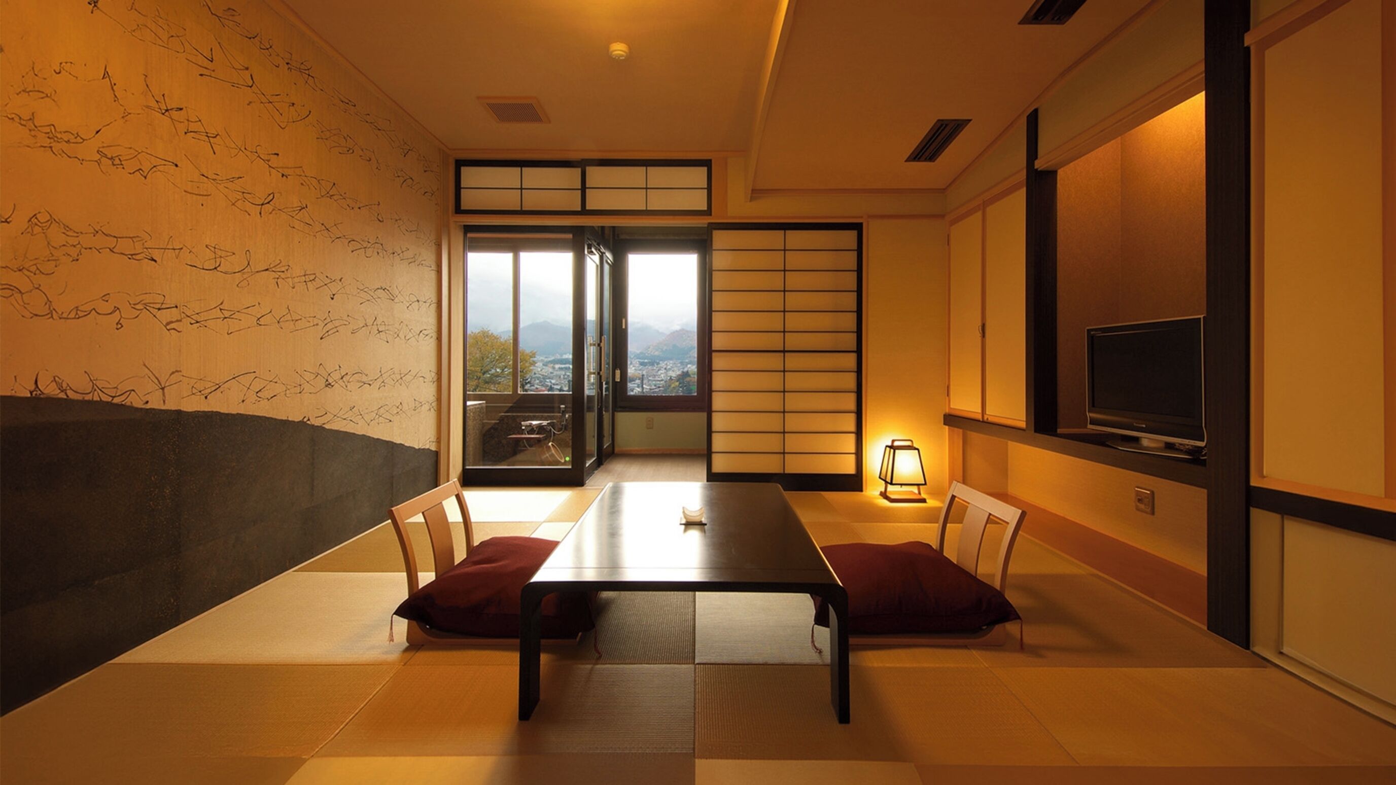 Una habitación japonesa tradicional con suelo de tatami, una mesa baja, puertas correderas, un televisor y vistas a un paisaje urbano.