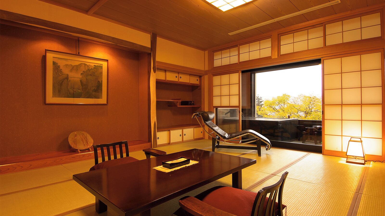 Una habitación japonesa tradicional con suelo de tatami, una mesa baja, un sillón acolchado y puertas correderas.
