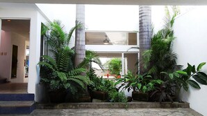 A courtyard with potted plants and a stone floor, surrounded by white walls and a glass door.