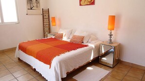 A bedroom with a bed, two bedside tables, a nightstand, a mirror, a window, and artwork on the walls.
