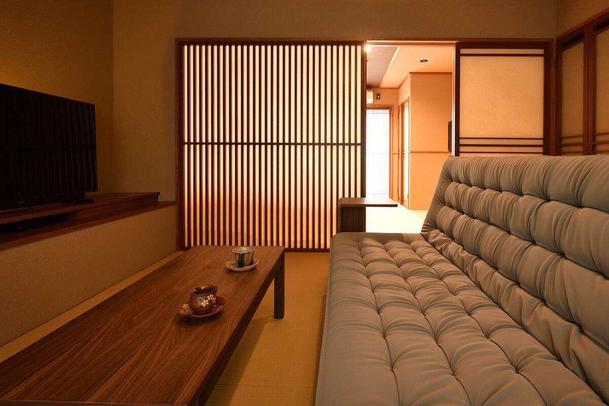 Una habitación tradicional japonesa con suelo de tatami, una baja mesita de madera con una taza y plato, un sofá acolchado y puertas correderas shoji.