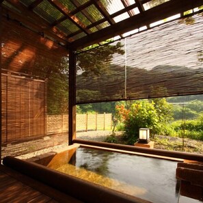 A traditional Japanese room with tatami flooring, a wooden bench, a small hot spring bath, and a view of greenery outside. - Shikinosato Kikuya (Sekikawa)
