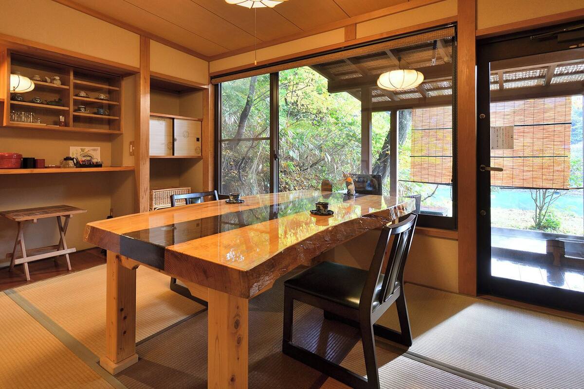 Una habitación tradicional japonesa con suelo de tatami, una mesa de madera para comer y un amplio ventanal con vistas a zonas verdes.