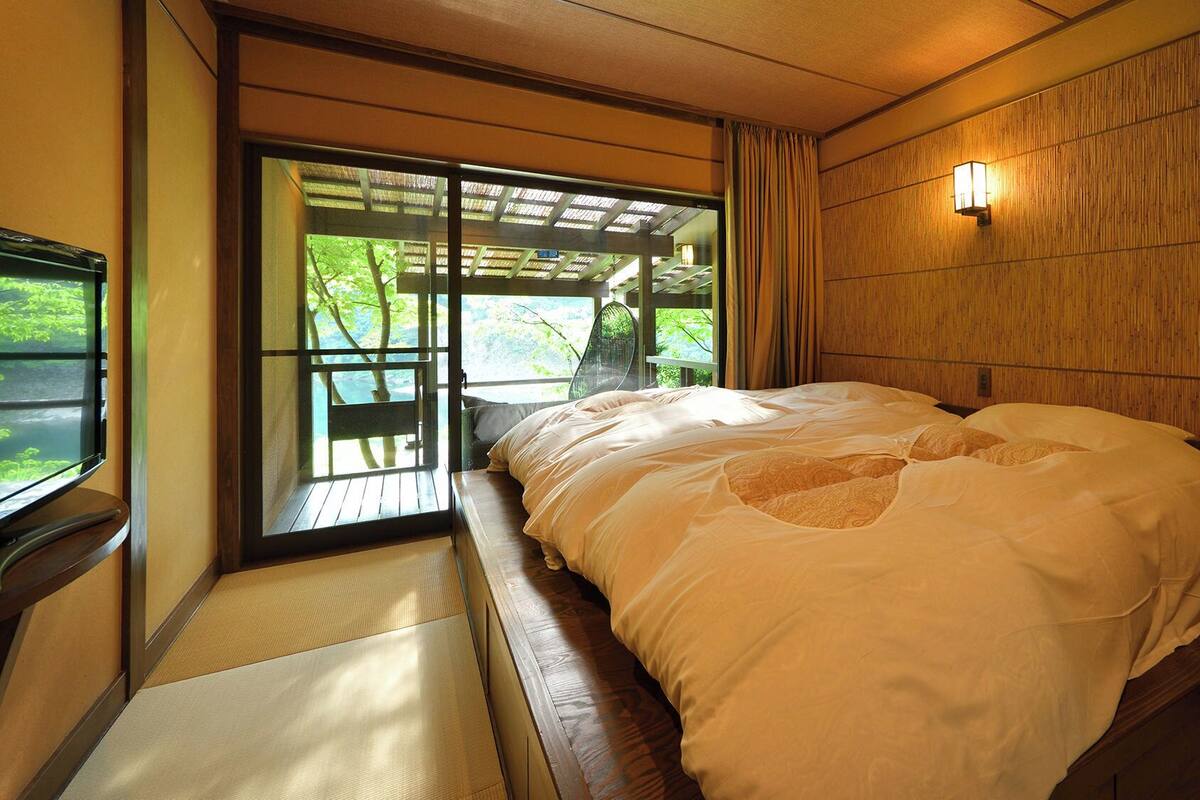 Un dormitorio con cama, ventana y vista a la vegetación.