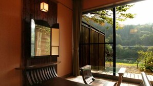 A room with a wooden bench, a small table, and a large window offering a view of greenery. - Shikinosato Kikuya (Sekikawa)
