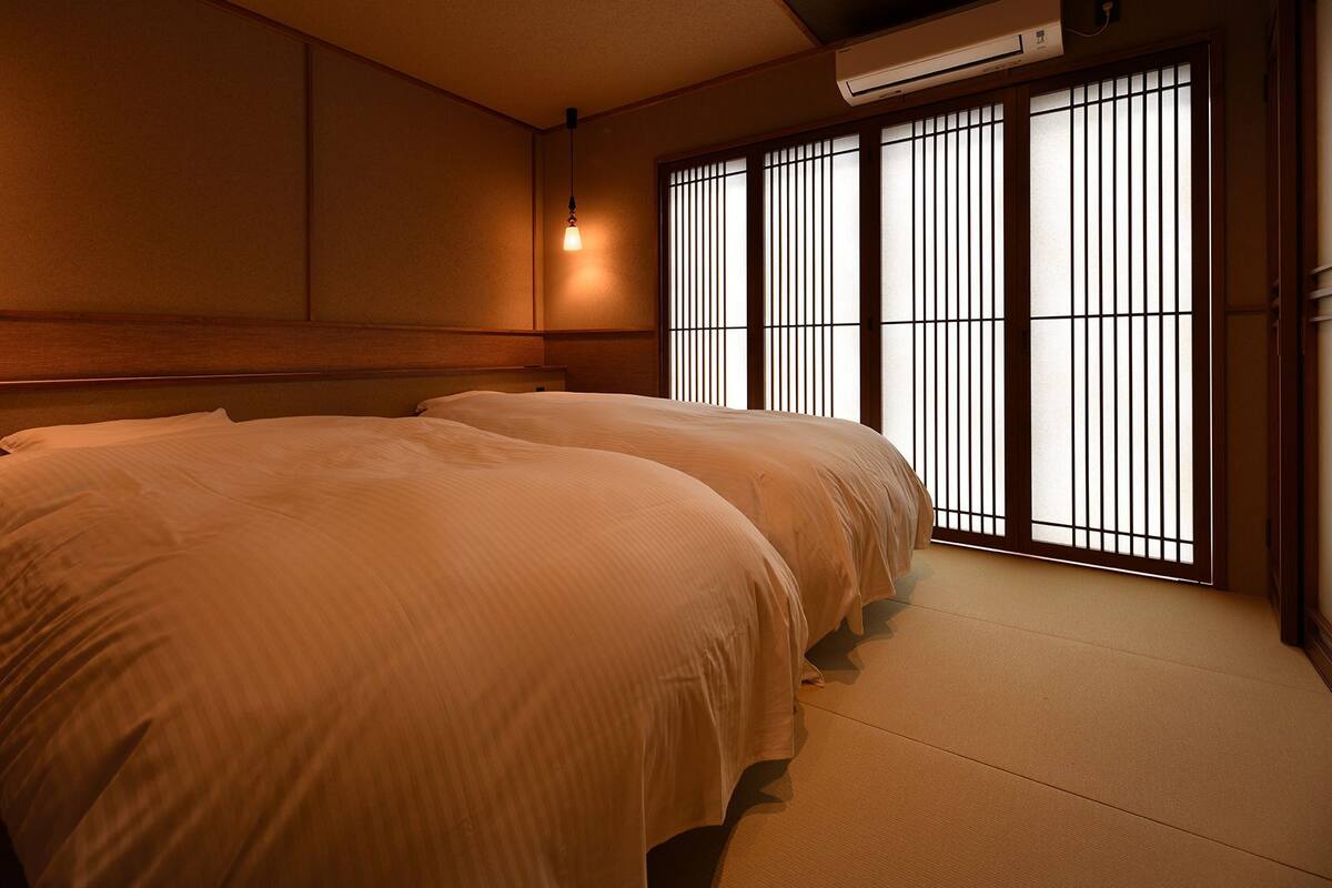 Una habitación con dos camas, una puerta corredera con paneles de shoji y un ventilador de techo.