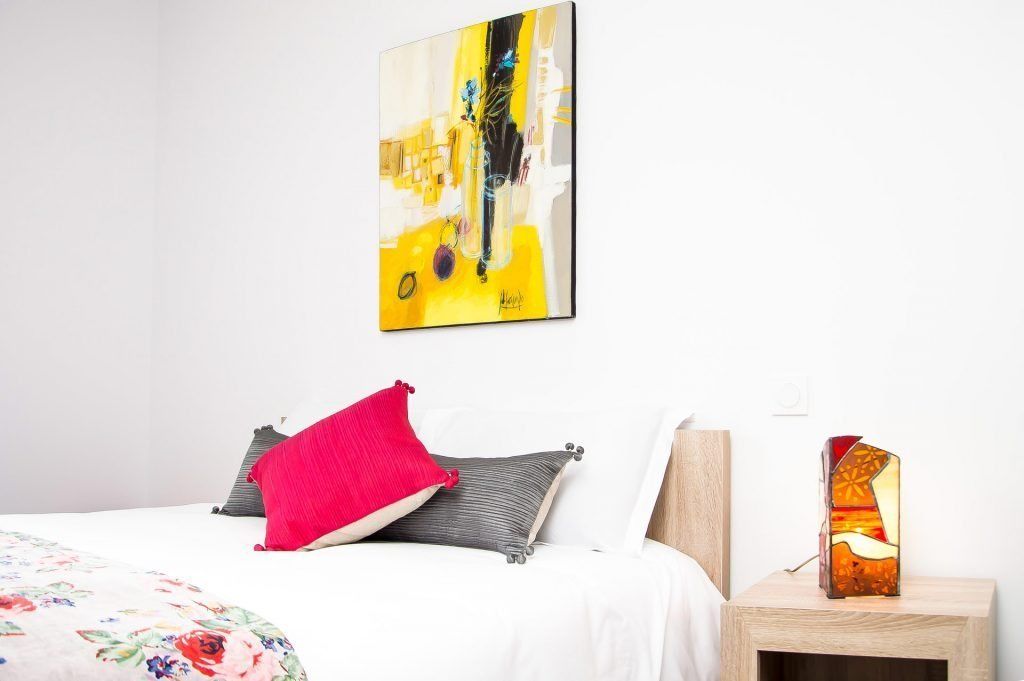 A bedroom with a bed, pillows, a nightstand, and a wall art piece.
