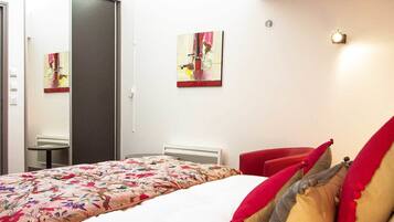 A bedroom with a bed, a red chair, and two paintings on the wall.