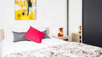 Une chambre à coucher avec un lit, un oreiller rouge, une couvre-lit à motifs floraux, une table de chevet avec une lampe et un tableau accroché au mur.