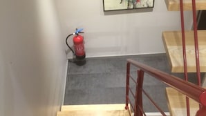 Una escalera de madera con barandilla roja que lleva a una plataforma. Un extintor está montado en la pared a la izquierda.