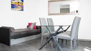 Un salón moderno con una mesa de comedor de vidrio, sillas grises, un sofá gris y un cojín rojo y gris. Un espejo grande cuelga de la pared sobre la mesa.