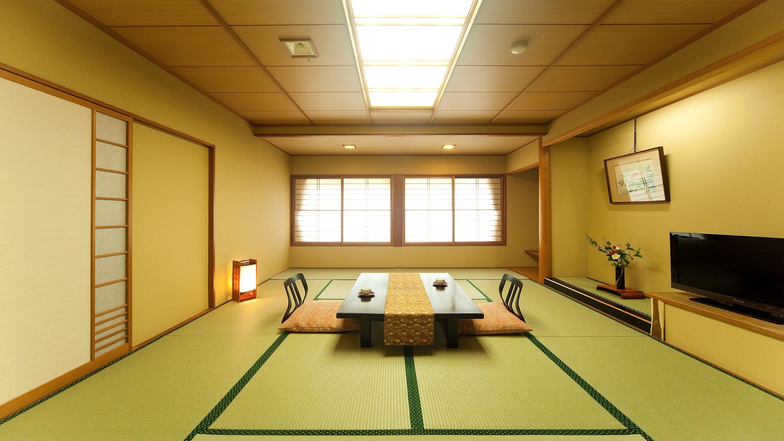 A tatami mat room with a low table, chairs, a television, and a sliding door.