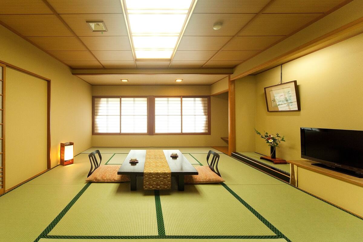 Una habitación con tatami, una mesa baja, sillas, un televisor y un fusil interior corredizo.