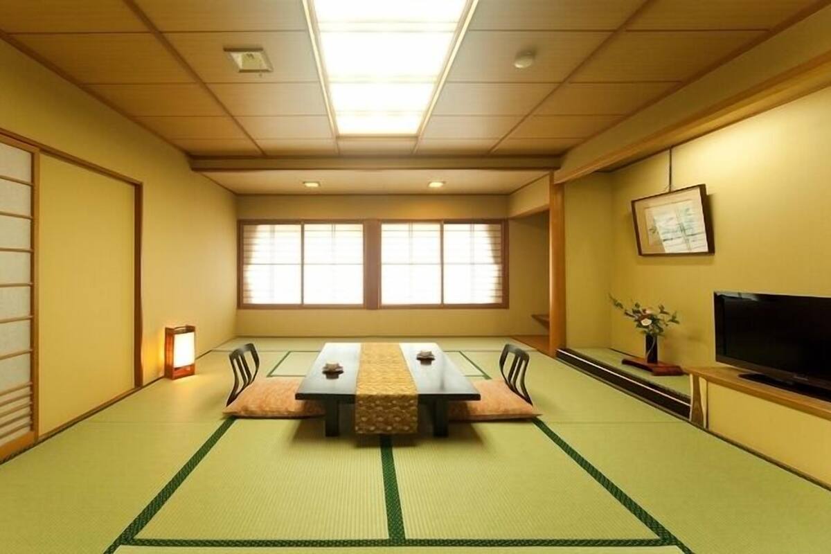 Una habitación con esteras tatami, una mesa baja, sillas, un televisor y una ventana.
