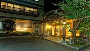 Um edifício japonês tradicional com fachada de madeira, um candeeiro de pedra e um jardim bem cuidado.