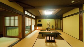 Um quarto japonês tradicional com tatames, uma mesa baixa, uma televisão e portas deslizantes.