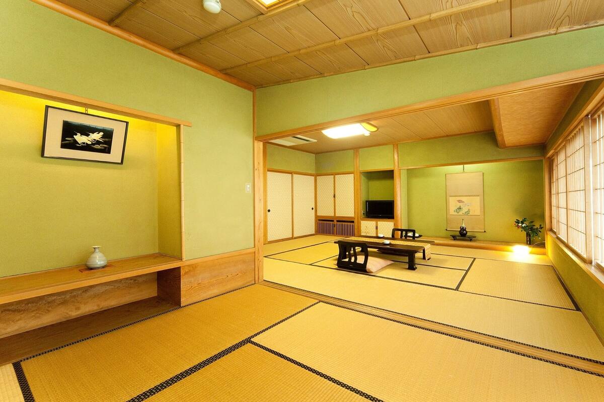 Una habitación con tatami, una mesa baja, un banco, una estantería con un florero y un cuadro en la pared.