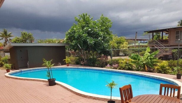 A swimming pool with a wooden deck, surrounded by potted plants and a wooden table with chairs. - Hibiscus Tabua Villas (Nadi)
