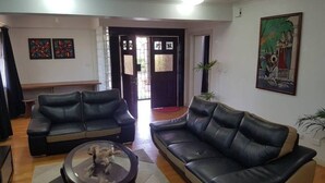 A living room with two black leather sofas, a coffee table, and a door leading to another room. There are two framed artworks on the wall and a potted plant. - Hibiscus Tabua Villas (Nadi)