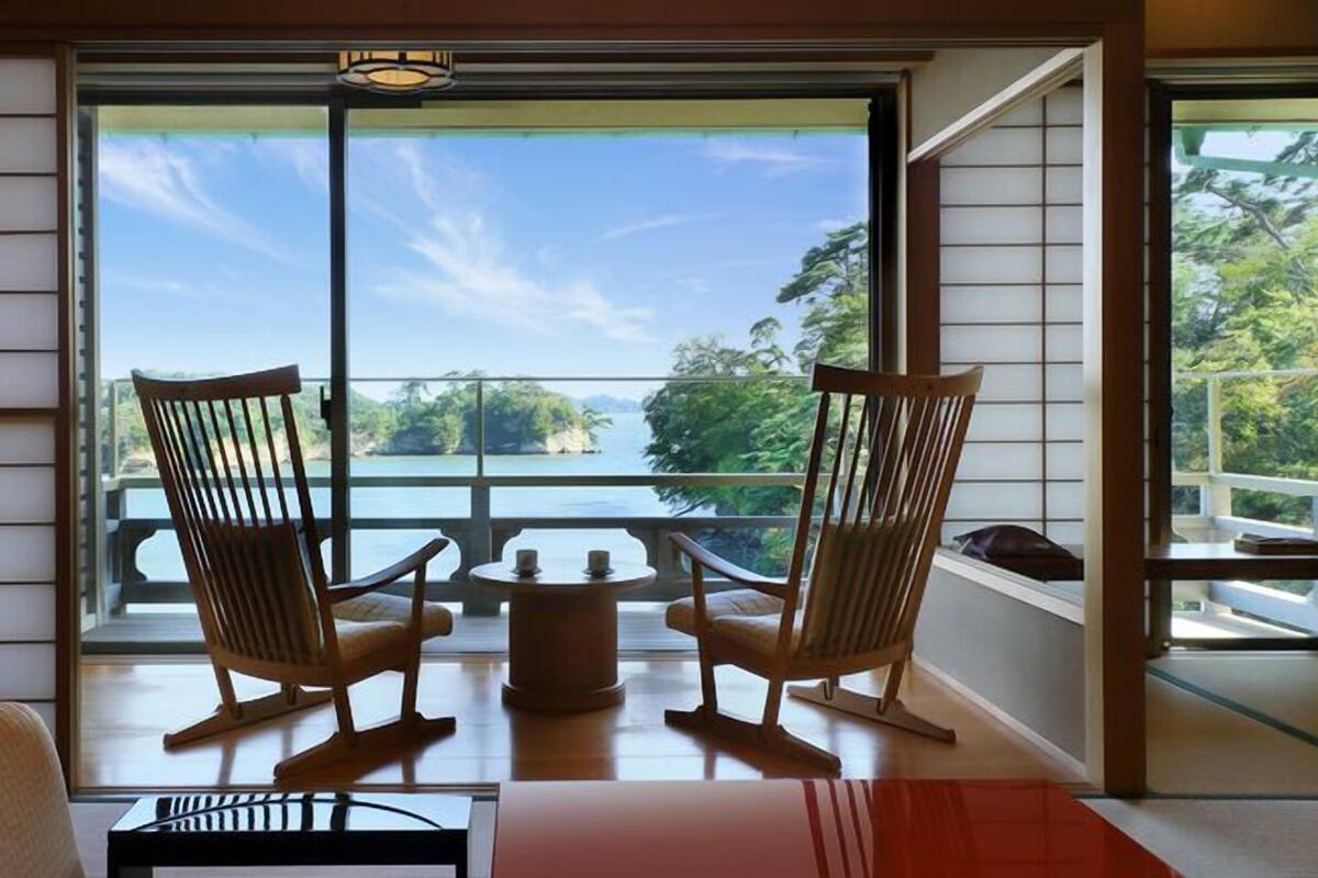 Una habitación con dos mecedoras de madera orientadas a un balcón con vistas a un lago y árboles.