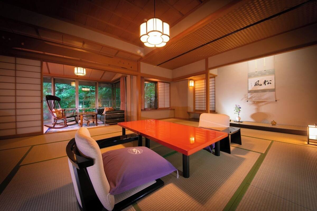 Una habitación japonesa tradicional con suelo de tatami, una mesa baja y un área de estar con cojines.