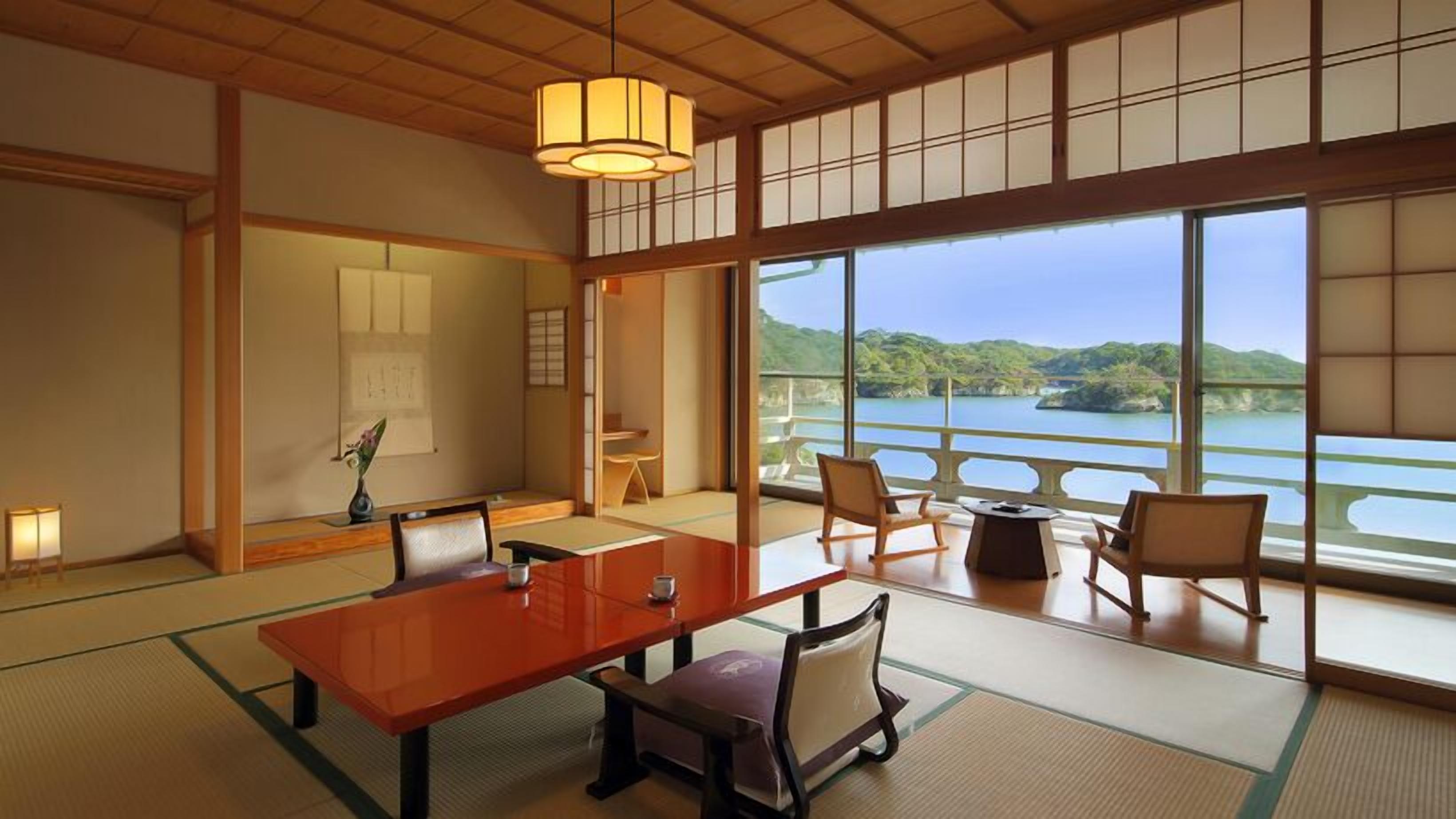 A traditional Japanese room with tatami flooring, a low table, chairs, and a view of a lake.