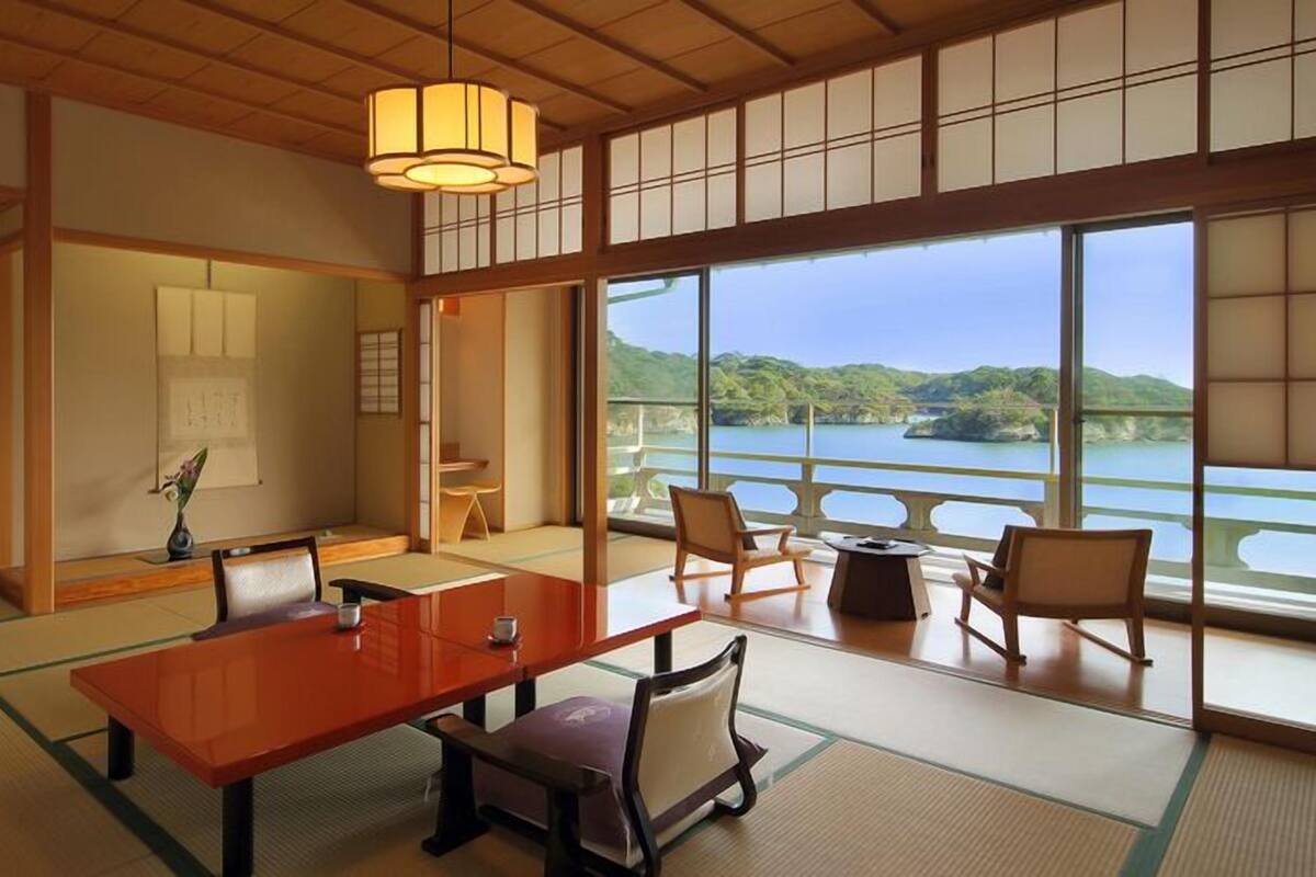 Una habitación tradicional japonesa con suelo de tatami, una mesa baja, sillas y vistas a un lago.