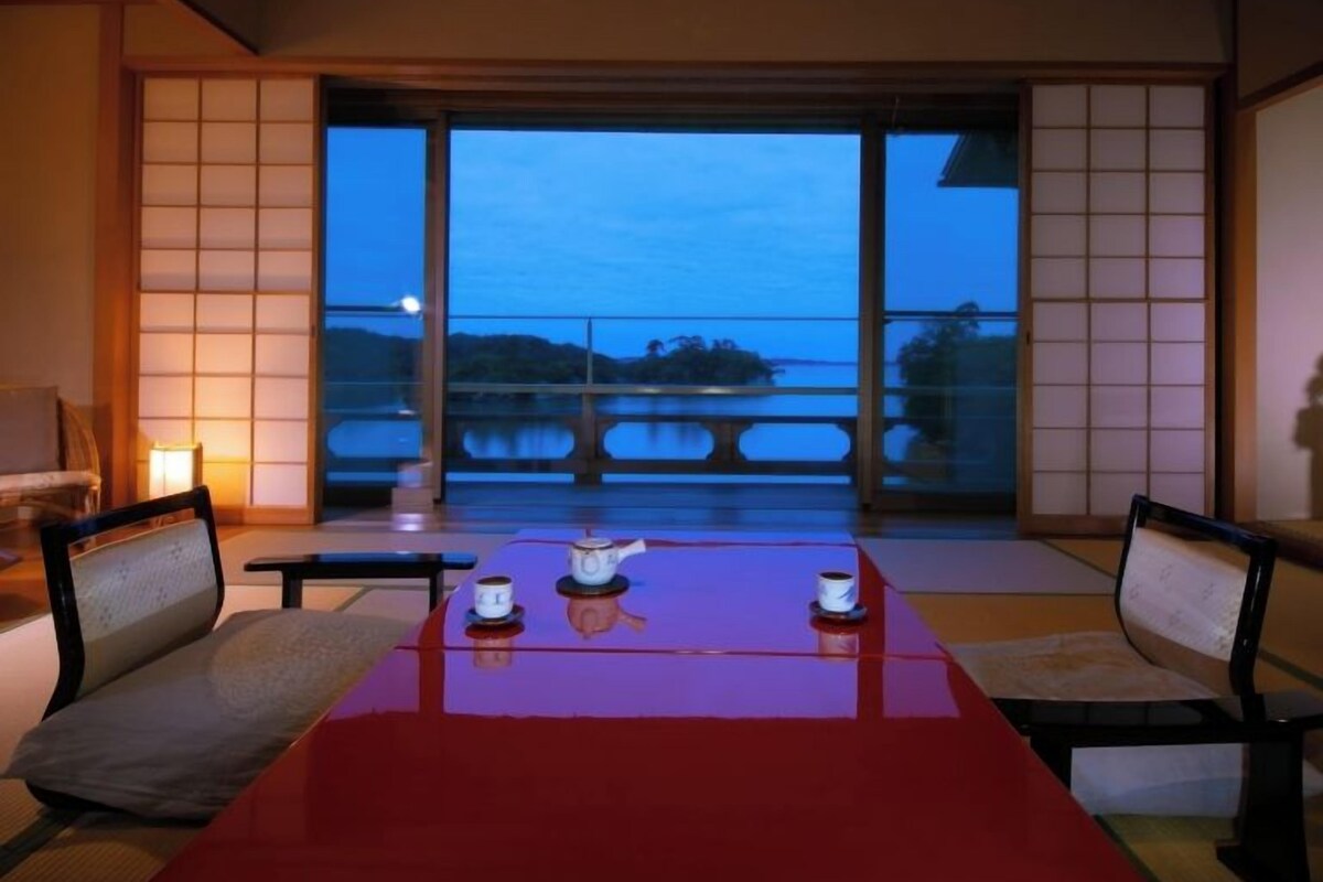 A room with a large sliding glass door, a red table with two cups and a teapot, and traditional Japanese sliding doors.