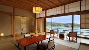 Um quarto japonês tradicional com tatames, uma mesa baixa, cadeiras e vista para um lago.