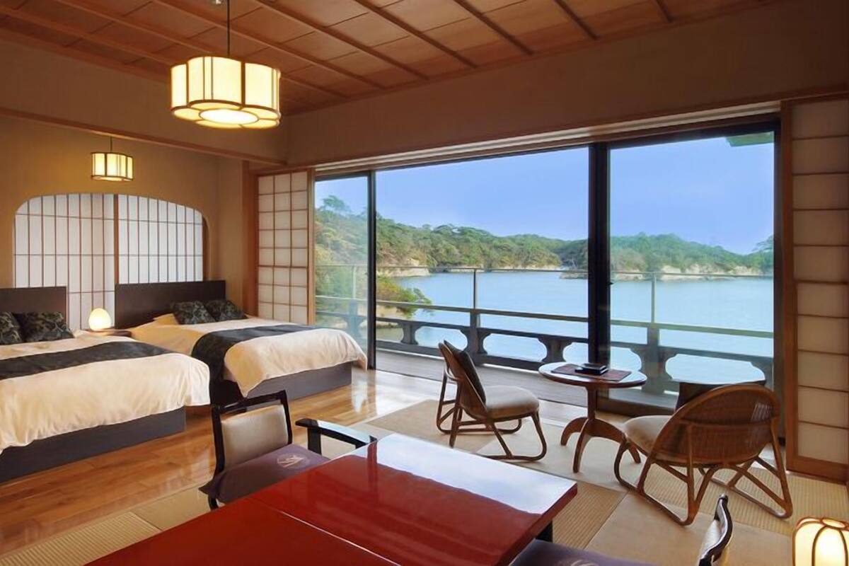 Habitación de hotel con dos camas, una mesa de comedor, sillas, vista a un lago y un balcón.