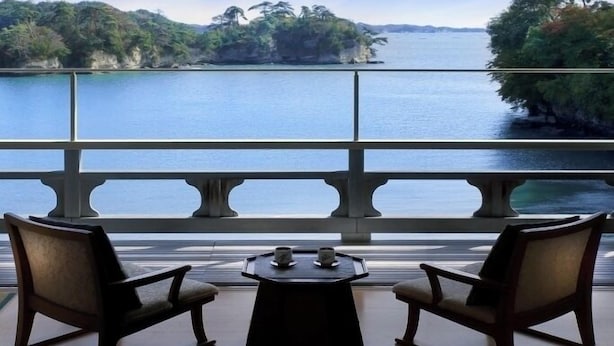Quarto com vista para um lago, duas cadeiras e uma mesa pequena.