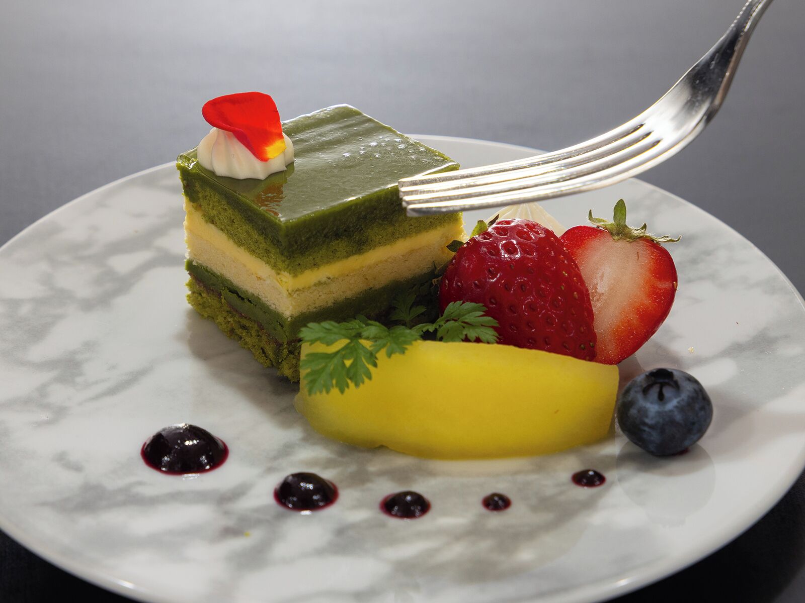 A dessert with a green layer, strawberries, a yellow fruit, and blueberries on a plate.