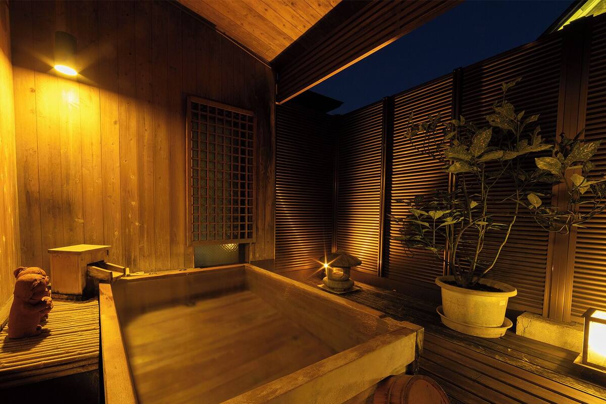A wooden spa area with a hot tub, a small table, and a potted plant.