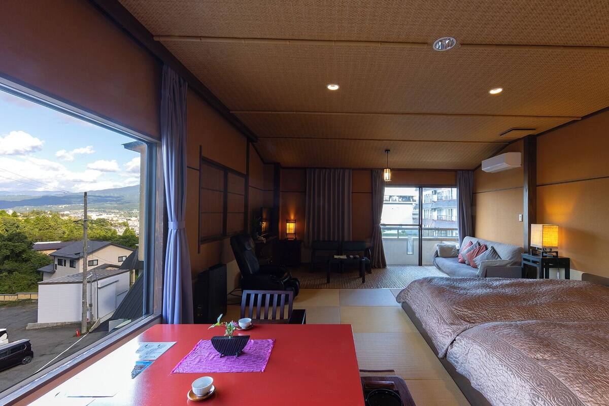 A hotel room with a bed, a desk with a chair, a sofa, and a view of the city.