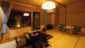 Una habitación tradicional japonesa con suelo de tatami, una mesa baja con cojines y una lámpara colgante.